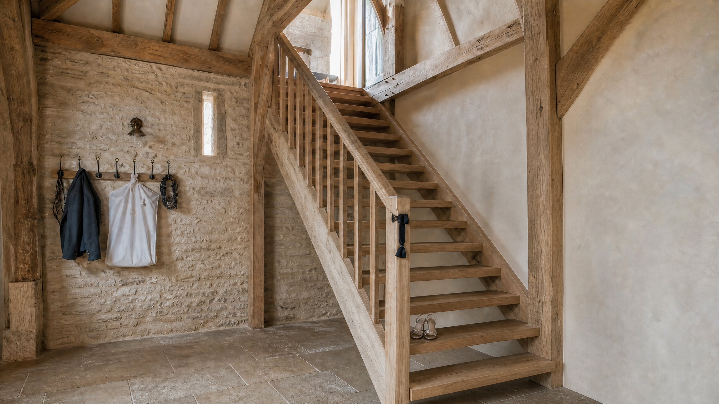 The open-tread oak stair from the barn floor up to the hayloft, jackets on iron hooks and party shoes at the foot